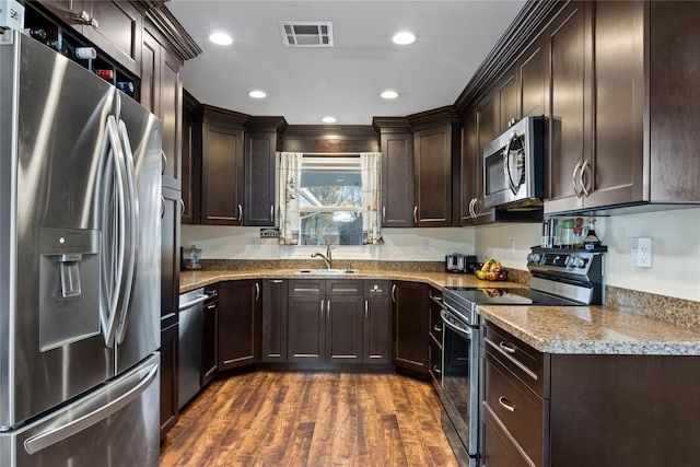 kitchen featuring appliances with stainless steel finishes, dark hardwood / wood-style flooring, dark brown cabinets, light stone countertops, and sink