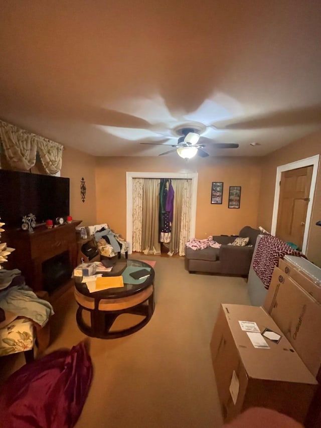 carpeted living room with a stone fireplace and ceiling fan