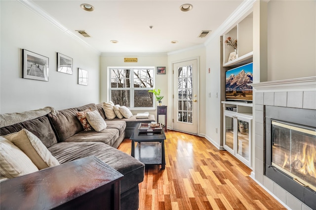 living room featuring light wood-type flooring, a tile fireplace, and crown molding