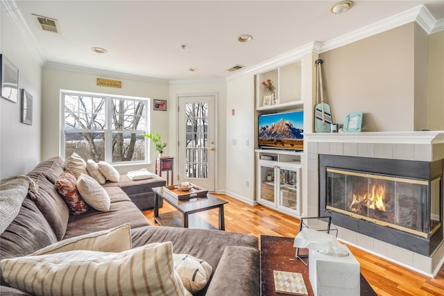 living room featuring a tiled fireplace, ornamental molding, and wood-type flooring