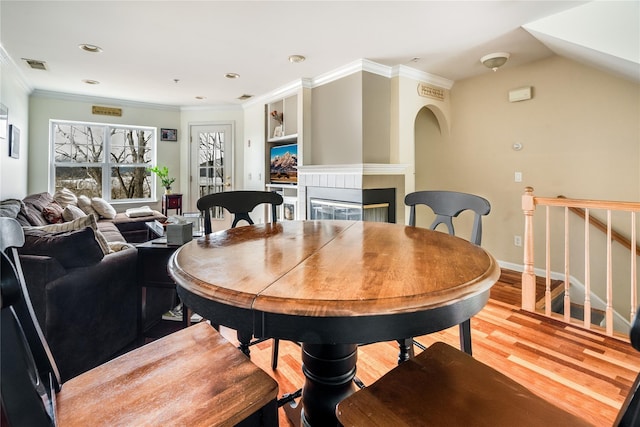 dining space featuring ornamental molding, a multi sided fireplace, and light hardwood / wood-style floors