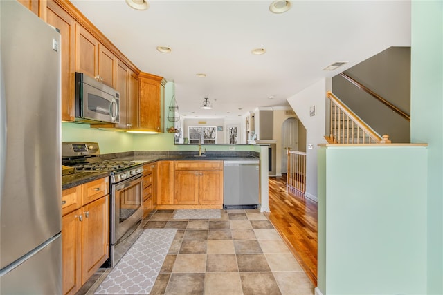 kitchen with light hardwood / wood-style flooring, dark stone countertops, kitchen peninsula, and appliances with stainless steel finishes