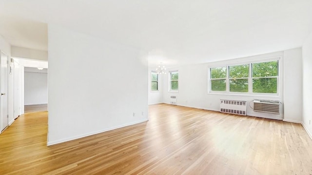 unfurnished living room featuring radiator, a chandelier, light wood-type flooring, and baseboards