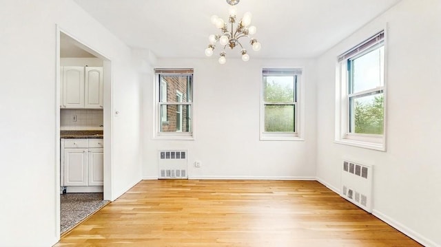 unfurnished dining area featuring radiator, a chandelier, and light wood finished floors