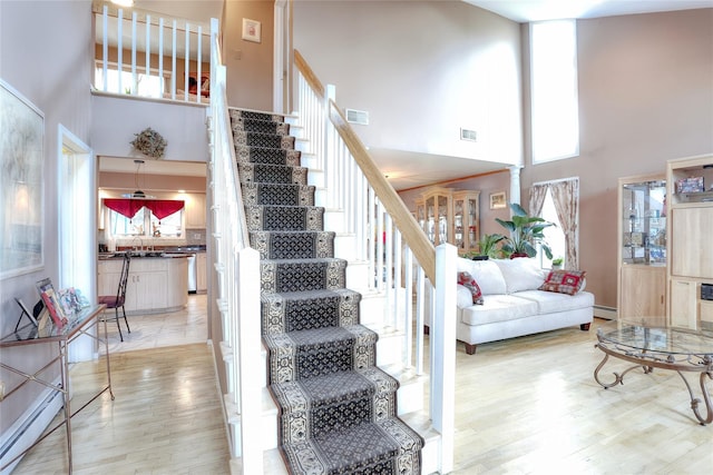 stairway featuring hardwood / wood-style floors, a towering ceiling, baseboard heating, and sink