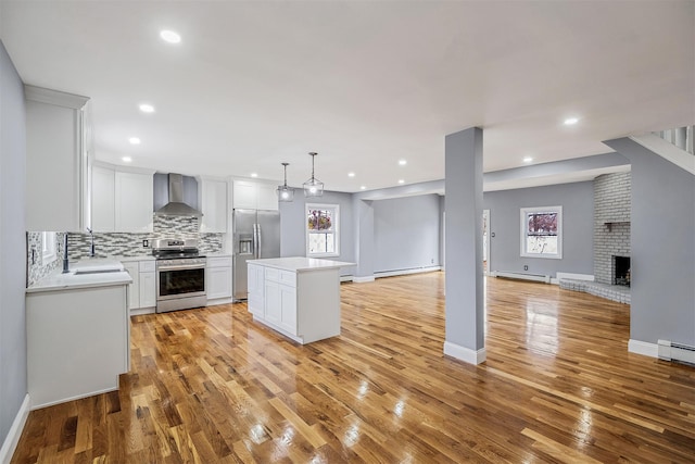 kitchen featuring wall chimney range hood, a kitchen island, backsplash, white cabinets, and appliances with stainless steel finishes