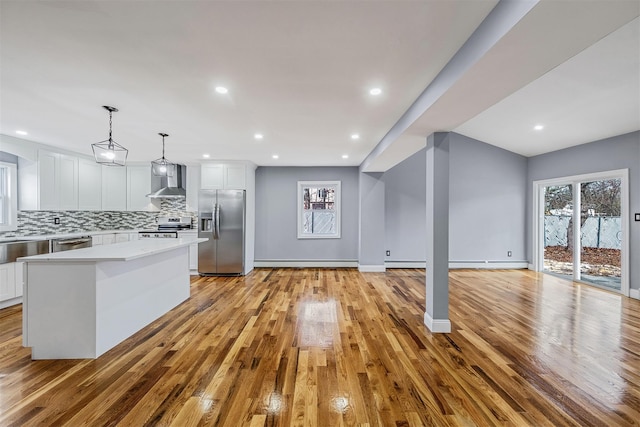 kitchen featuring a center island, stainless steel appliances, wall chimney range hood, pendant lighting, and white cabinets