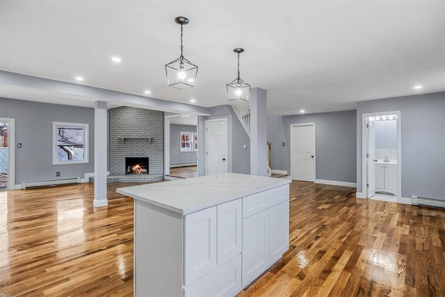 kitchen with light stone countertops, white cabinetry, a baseboard radiator, pendant lighting, and a fireplace