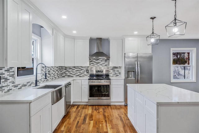 kitchen with stainless steel appliances, sink, wall chimney range hood, decorative light fixtures, and white cabinets