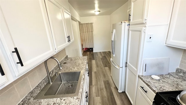 kitchen featuring sink, white cabinetry, light stone counters, white refrigerator, and hardwood / wood-style flooring