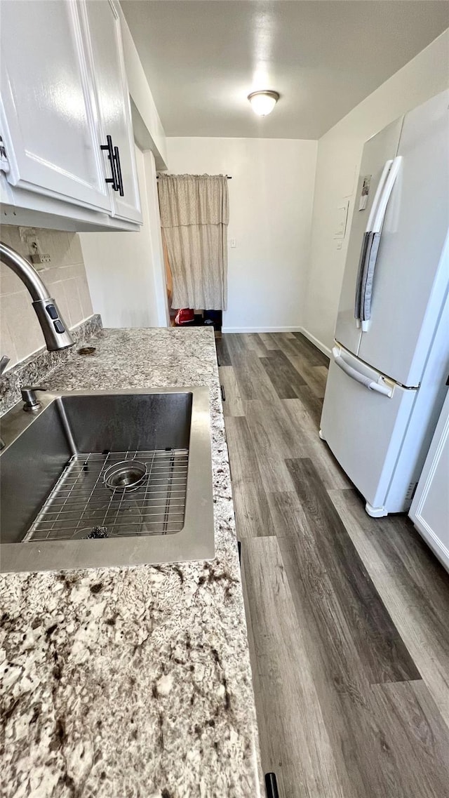 kitchen with sink, dark wood-type flooring, white cabinetry, light stone counters, and white fridge