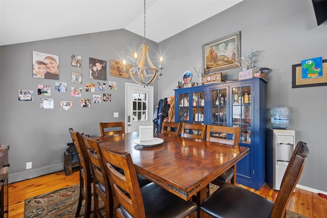 dining room with an inviting chandelier, hardwood / wood-style flooring, and vaulted ceiling