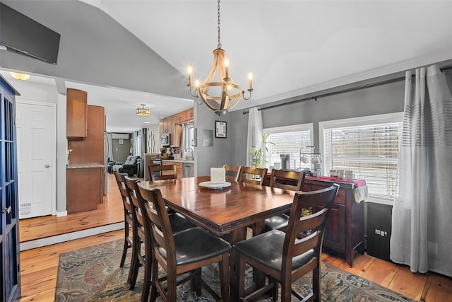 dining space with lofted ceiling, sink, light hardwood / wood-style flooring, and a chandelier