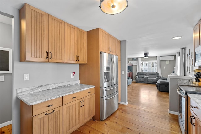 kitchen featuring appliances with stainless steel finishes, light stone counters, a wall mounted air conditioner, light hardwood / wood-style floors, and light brown cabinetry