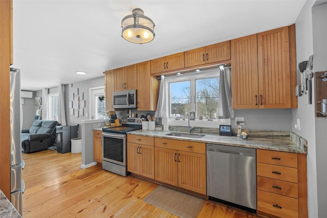 kitchen featuring light stone countertops, appliances with stainless steel finishes, sink, and light hardwood / wood-style flooring