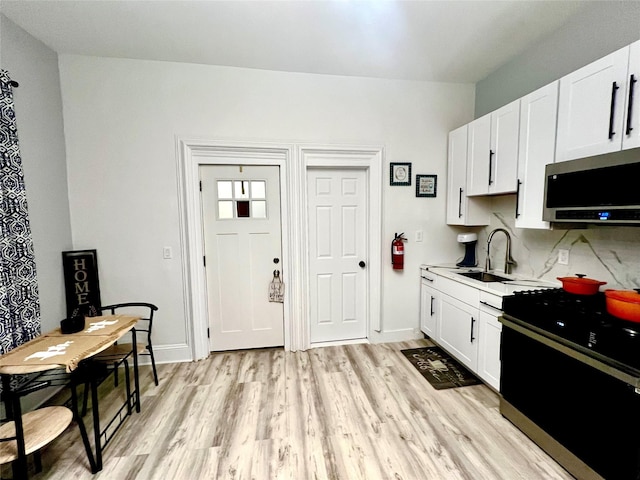 kitchen with black gas range oven, tasteful backsplash, white cabinetry, sink, and light wood-type flooring