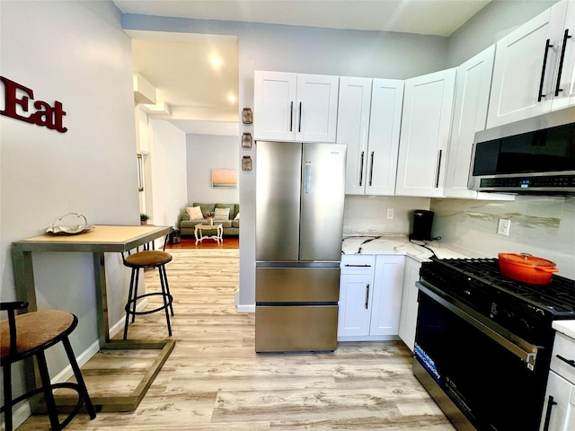 kitchen featuring light stone counters, light hardwood / wood-style flooring, a kitchen breakfast bar, stainless steel appliances, and white cabinets