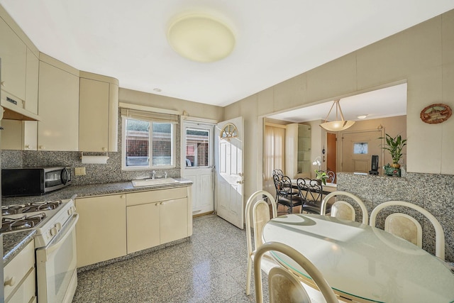 kitchen featuring cream cabinets, decorative light fixtures, white gas stove, and sink