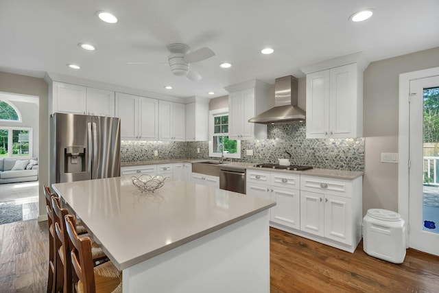 kitchen with white cabinets, wall chimney exhaust hood, plenty of natural light, a kitchen island, and stainless steel appliances