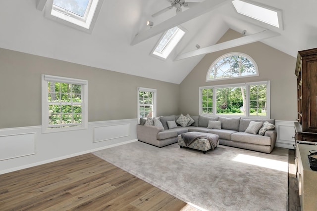 living room with a skylight, ceiling fan, beamed ceiling, and wood-type flooring