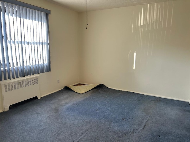 empty room with radiator, a healthy amount of sunlight, and dark colored carpet