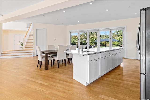 kitchen with a kitchen island with sink, white cabinets, sink, light wood-type flooring, and stainless steel refrigerator