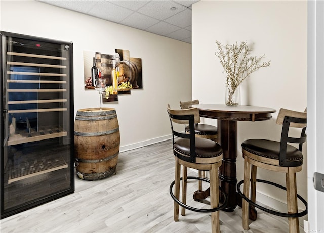 bar with a paneled ceiling, wood-type flooring, and beverage cooler