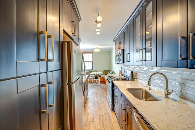 kitchen featuring sink, tasteful backsplash, light wood-type flooring, stainless steel appliances, and light stone countertops