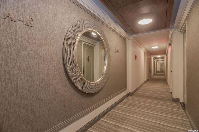 hall with carpet floors, a raised ceiling, and crown molding