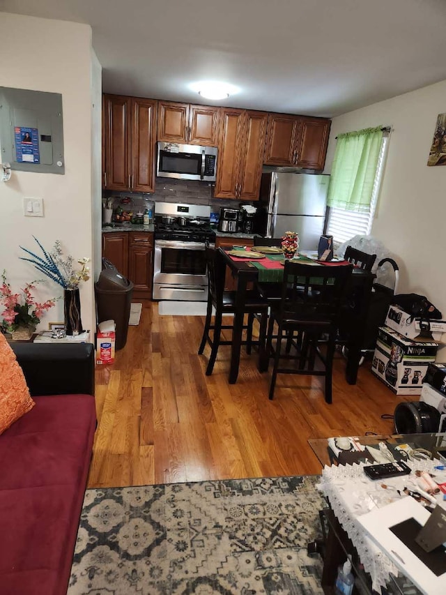 kitchen with electric panel, light hardwood / wood-style floors, appliances with stainless steel finishes, and tasteful backsplash