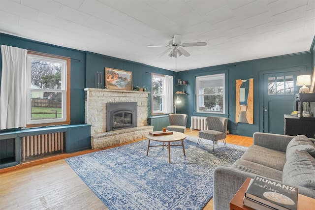 living room with a fireplace, radiator heating unit, ceiling fan, and light wood-type flooring