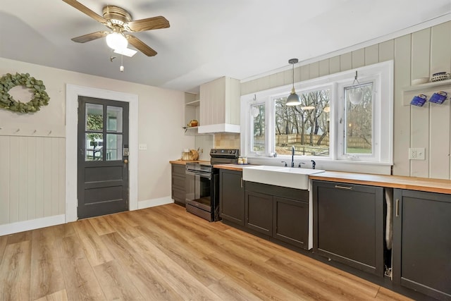 kitchen with custom range hood, hanging light fixtures, stainless steel range with electric stovetop, sink, and light hardwood / wood-style flooring