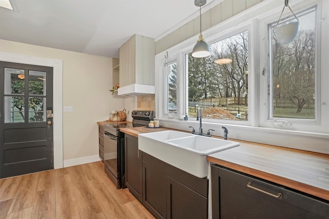 kitchen featuring wood counters, decorative light fixtures, black range with electric stovetop, light hardwood / wood-style floors, and sink