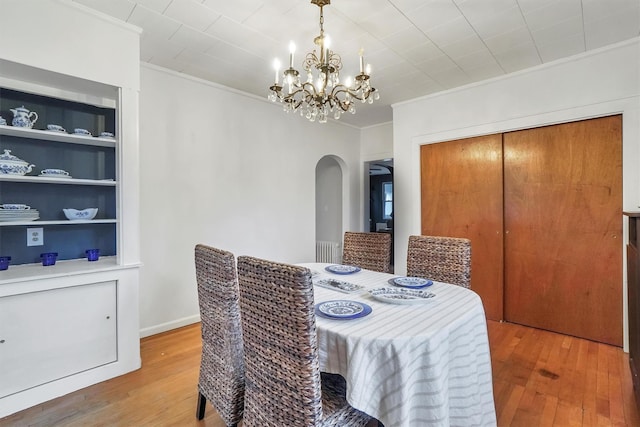 dining space featuring built in shelves, crown molding, an inviting chandelier, and hardwood / wood-style flooring