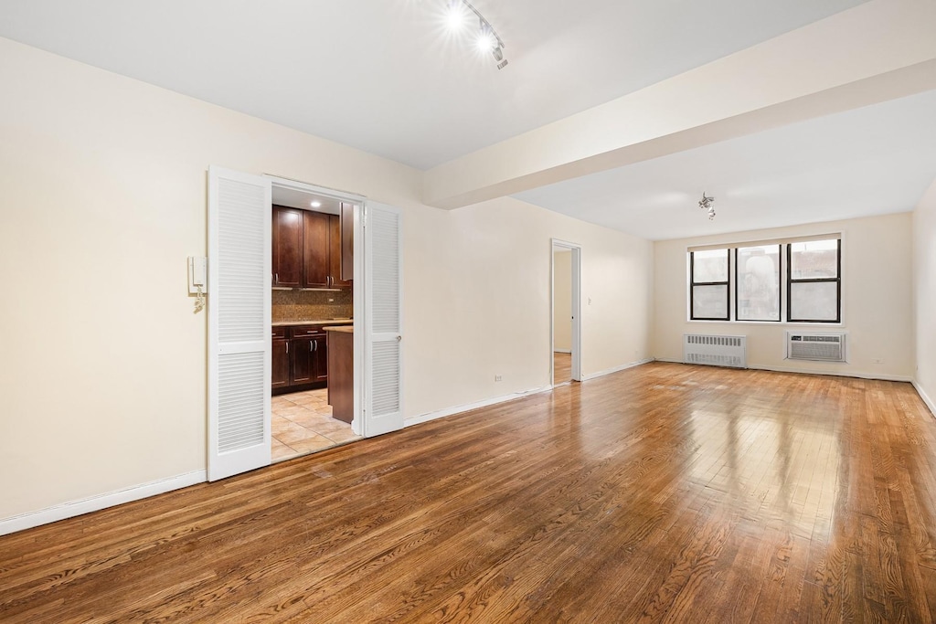 unfurnished room with light hardwood / wood-style flooring, radiator, and an AC wall unit