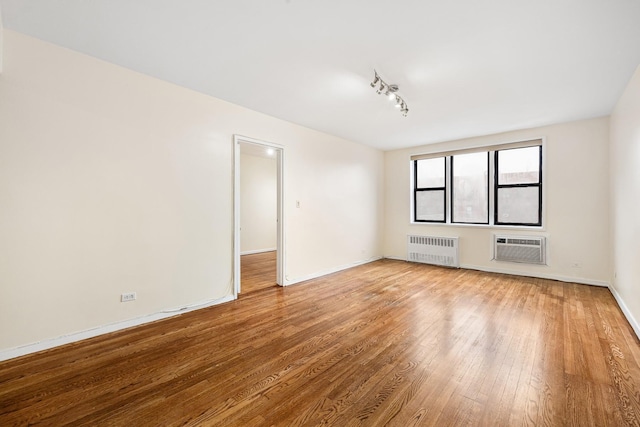 unfurnished room with hardwood / wood-style flooring, an AC wall unit, radiator, and track lighting