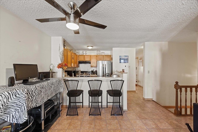 kitchen featuring a breakfast bar, ceiling fan, a textured ceiling, kitchen peninsula, and stainless steel refrigerator