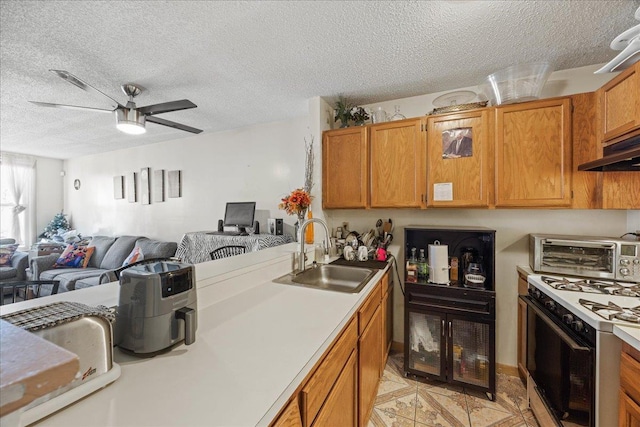 kitchen with a textured ceiling, white gas stove, ceiling fan, and sink