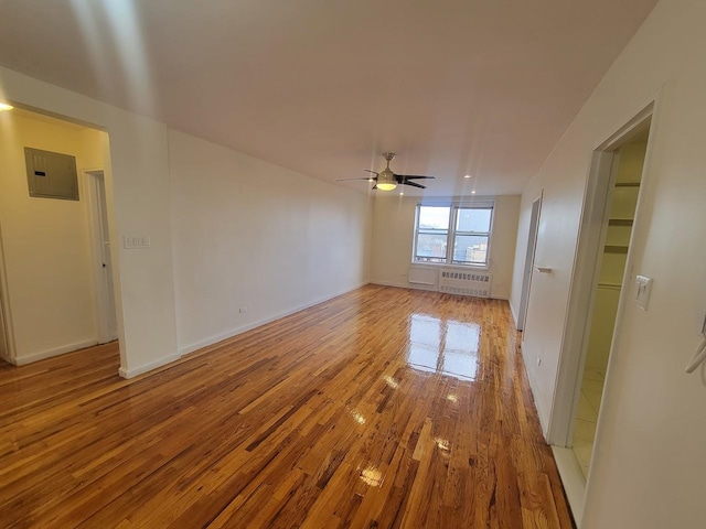 unfurnished room with ceiling fan, light hardwood / wood-style floors, radiator, and electric panel