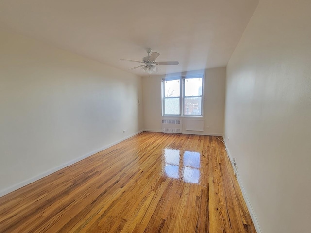 unfurnished room featuring ceiling fan, light wood-type flooring, and radiator