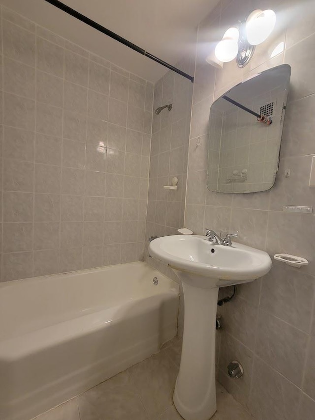 bathroom with tile patterned flooring, tiled shower / bath combo, tile walls, and sink