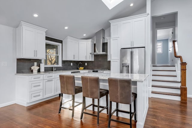 kitchen with wall chimney range hood, high quality fridge, white cabinetry, and a kitchen island