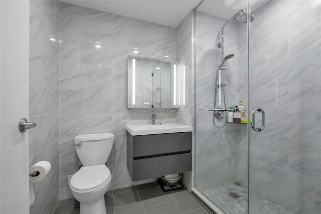 bathroom featuring tile patterned flooring, vanity, tile walls, toilet, and a shower with shower door