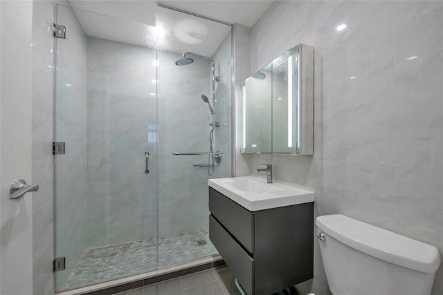 bathroom with an enclosed shower, tile patterned flooring, vanity, tile walls, and toilet