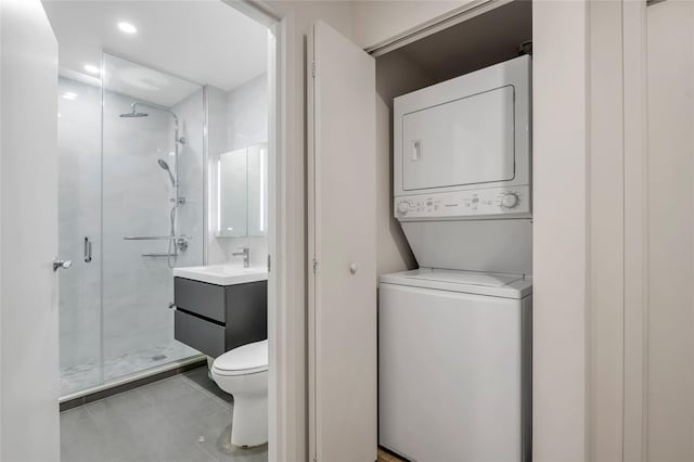 bathroom featuring toilet, tile patterned flooring, an enclosed shower, stacked washing maching and dryer, and vanity