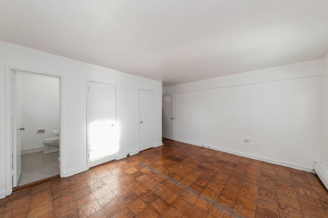 unfurnished bedroom with parquet flooring, a baseboard radiator, and ensuite bath