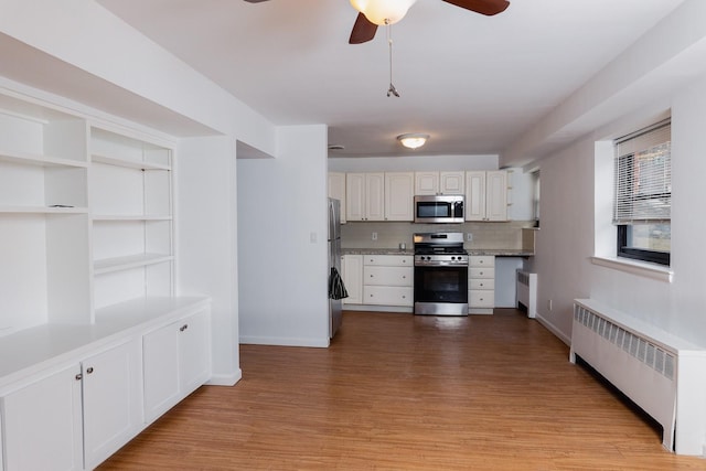 kitchen featuring light wood finished floors, radiator heating unit, appliances with stainless steel finishes, and ceiling fan