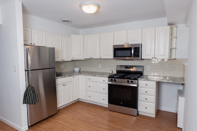 kitchen featuring backsplash, stainless steel appliances, white cabinets, and light wood-type flooring