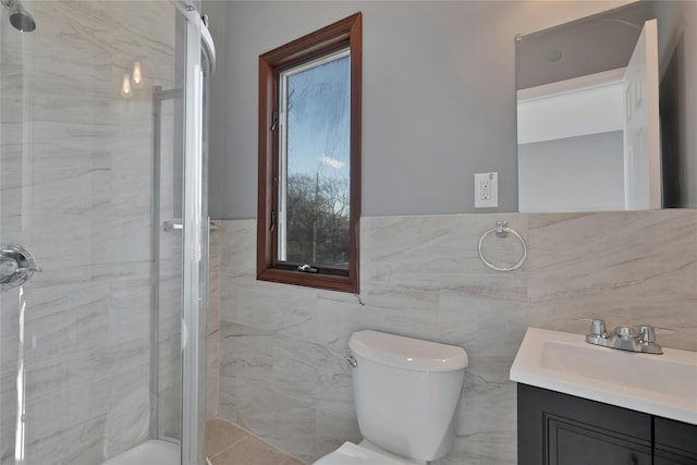 bathroom with vanity, toilet, a shower with shower door, and tile walls