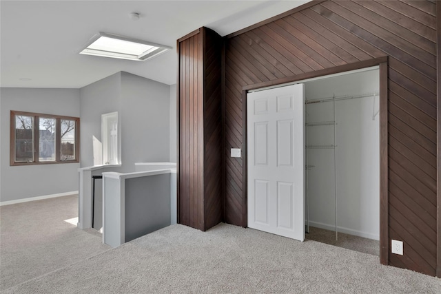 unfurnished bedroom featuring light carpet, a closet, lofted ceiling, and wood walls